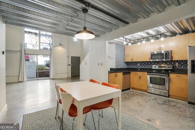 kitchen with appliances with stainless steel finishes, dark countertops, pendant lighting, and concrete floors