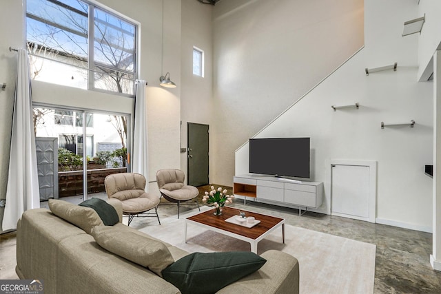 living area featuring baseboards, a healthy amount of sunlight, and a high ceiling