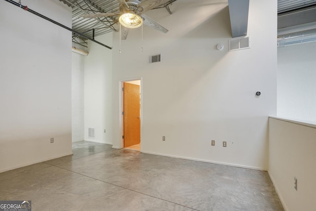 unfurnished room with visible vents, concrete floors, a towering ceiling, and ceiling fan