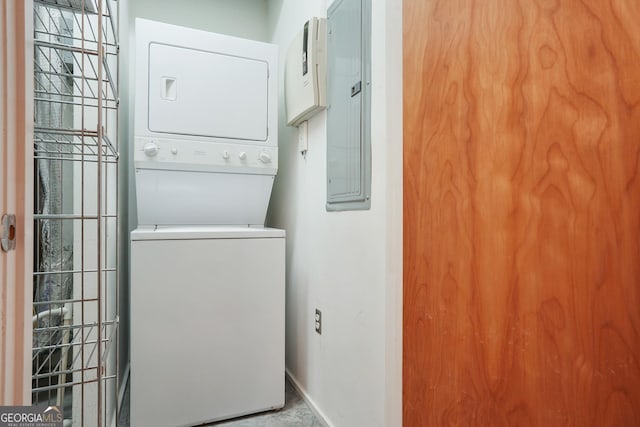 laundry room with electric panel, baseboards, and stacked washer / dryer