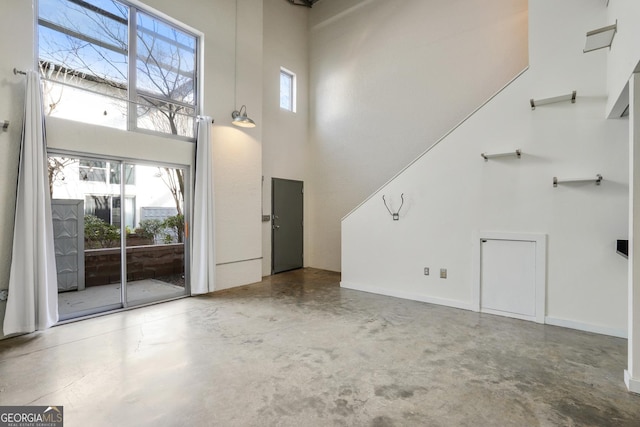 unfurnished living room with concrete flooring, baseboards, and a high ceiling