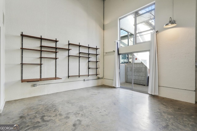 spare room with concrete flooring, a textured wall, and a towering ceiling