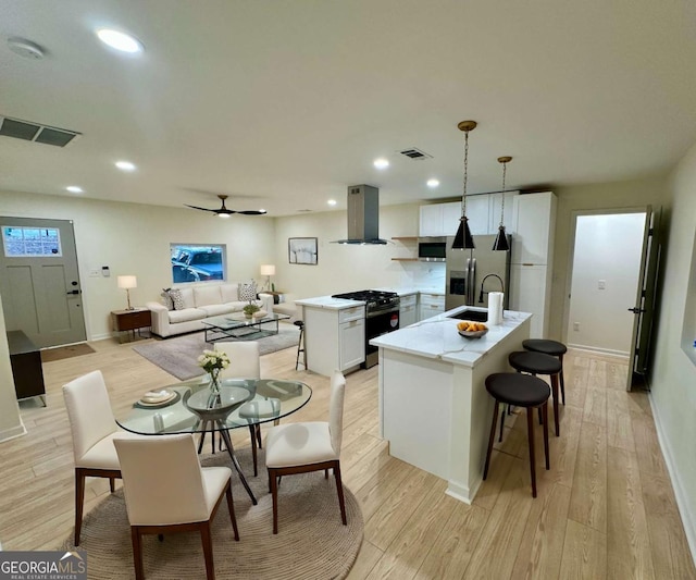 kitchen featuring island range hood, decorative light fixtures, a center island with sink, white cabinetry, and appliances with stainless steel finishes