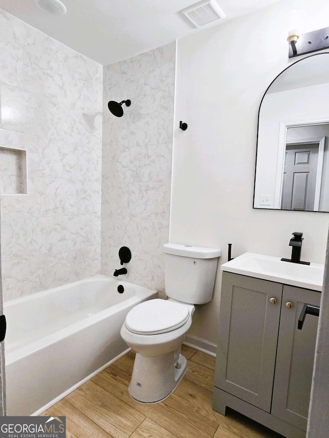 full bathroom with toilet, tiled shower / bath combo, wood-type flooring, and vanity