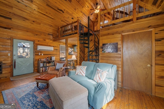 living room featuring ceiling fan, high vaulted ceiling, a wall unit AC, wood walls, and light hardwood / wood-style floors