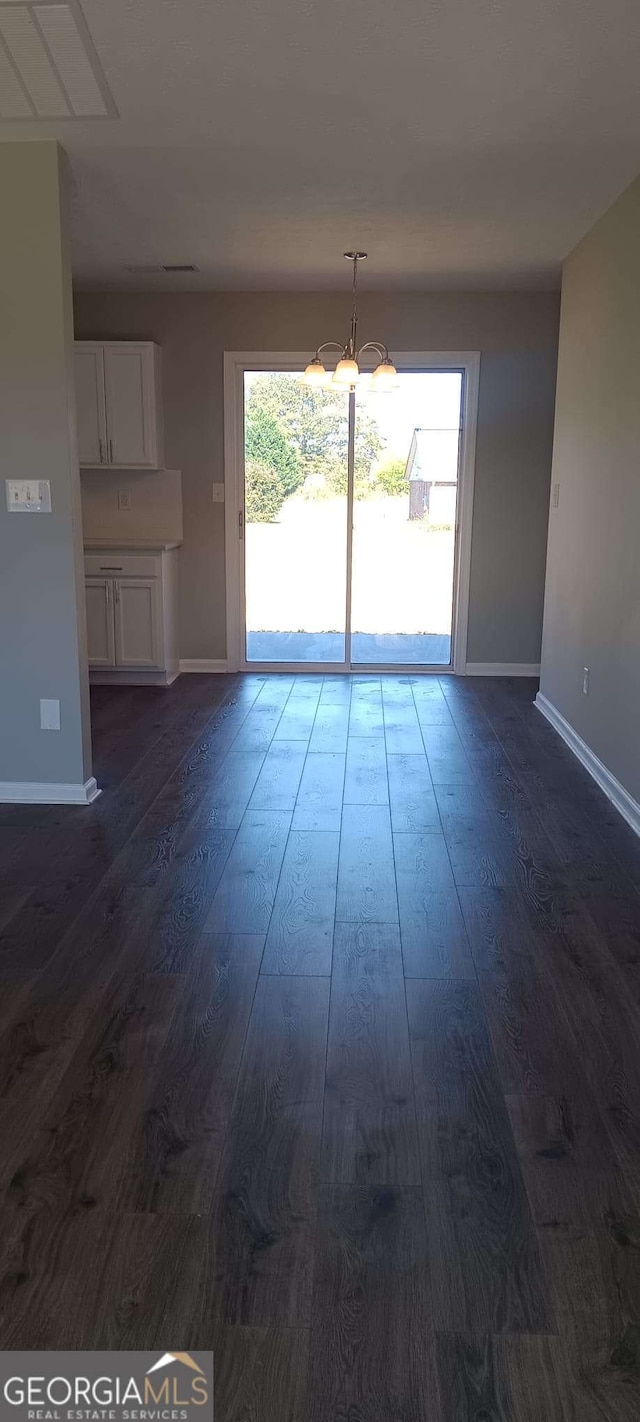 unfurnished living room featuring a chandelier, plenty of natural light, and dark wood-type flooring