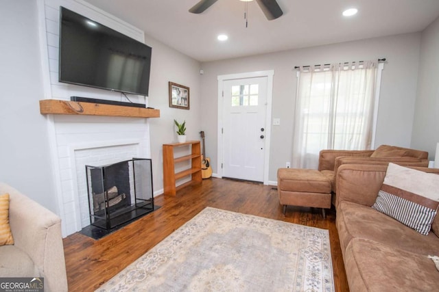 living room with a brick fireplace, ceiling fan, and dark wood-type flooring