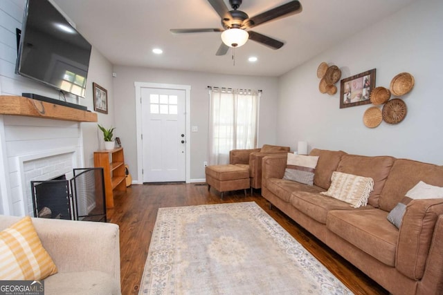 living room featuring ceiling fan, dark wood-type flooring, and a brick fireplace