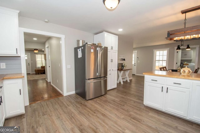 kitchen with white cabinets, light hardwood / wood-style flooring, ceiling fan, decorative light fixtures, and stainless steel refrigerator