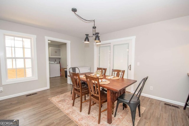 dining room featuring light wood-type flooring, washer / clothes dryer, and an inviting chandelier