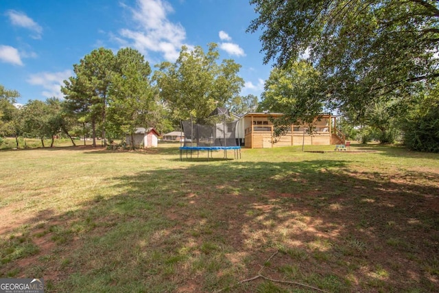 view of yard with a trampoline, a deck, and a storage unit