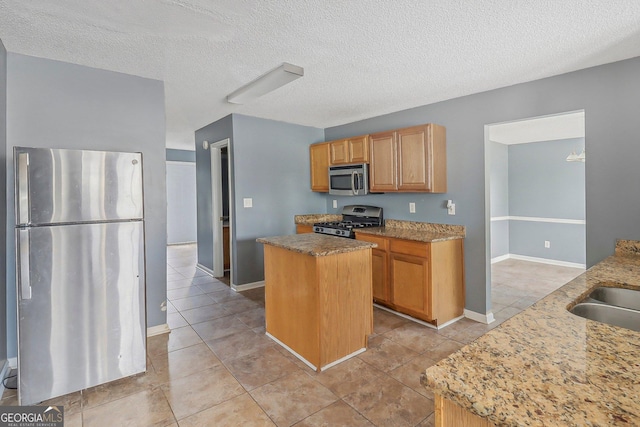 kitchen featuring light stone counters, a textured ceiling, stainless steel appliances, sink, and a kitchen island