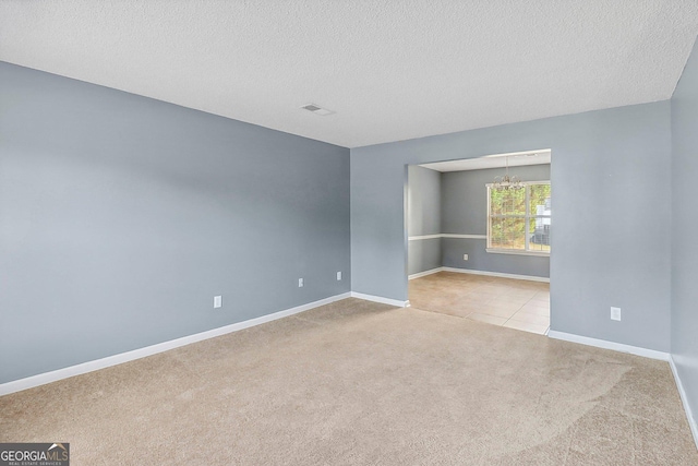 carpeted spare room with a textured ceiling and a notable chandelier