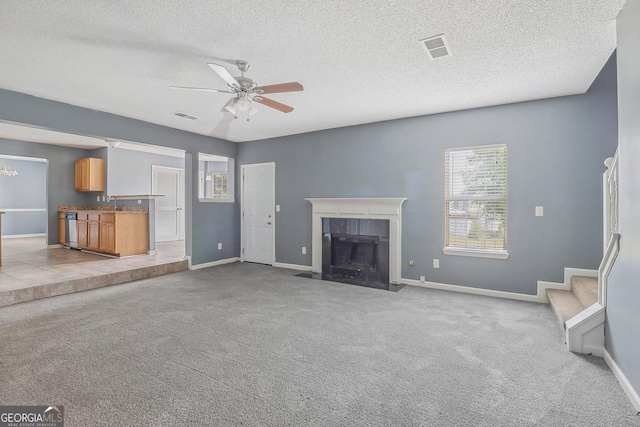 unfurnished living room featuring a fireplace, a textured ceiling, light colored carpet, and ceiling fan