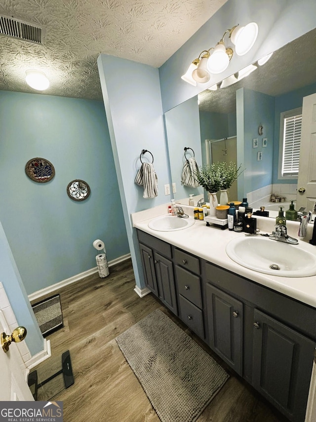 bathroom featuring wood-type flooring, shower with separate bathtub, vanity, and a textured ceiling