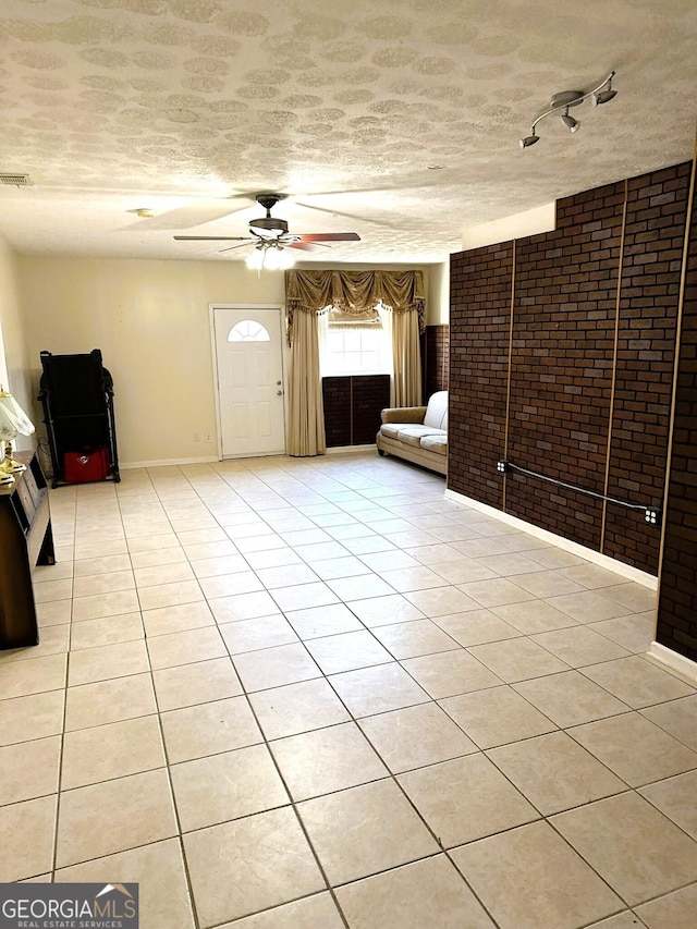 unfurnished living room featuring light tile patterned flooring, ceiling fan, brick wall, and a textured ceiling