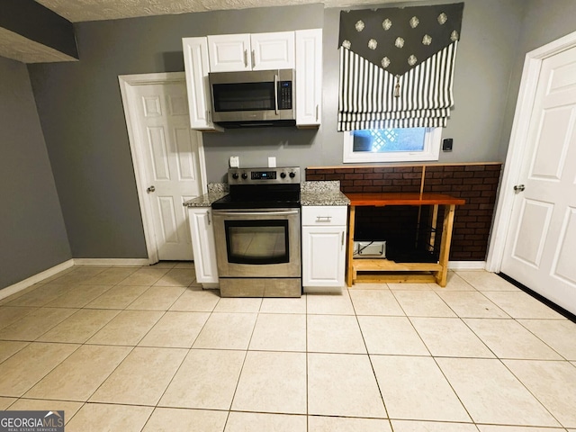 kitchen with light tile patterned floors, appliances with stainless steel finishes, white cabinetry, a textured ceiling, and dark stone counters