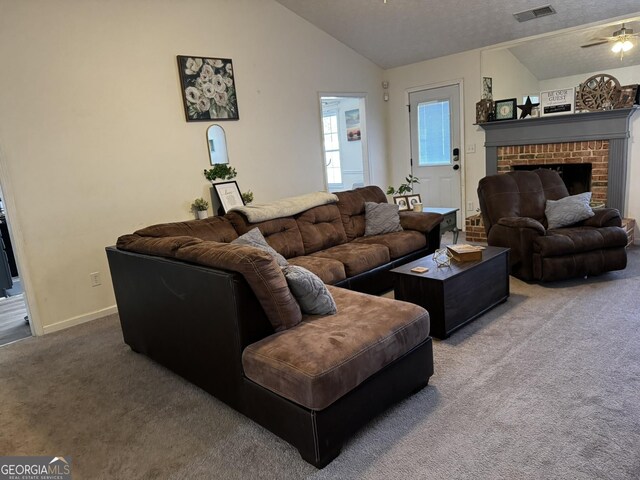 carpeted living room featuring ceiling fan, lofted ceiling, a brick fireplace, and a textured ceiling