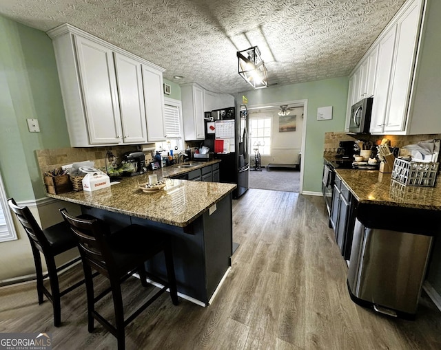 kitchen with dark stone countertops, a breakfast bar, kitchen peninsula, and white cabinets