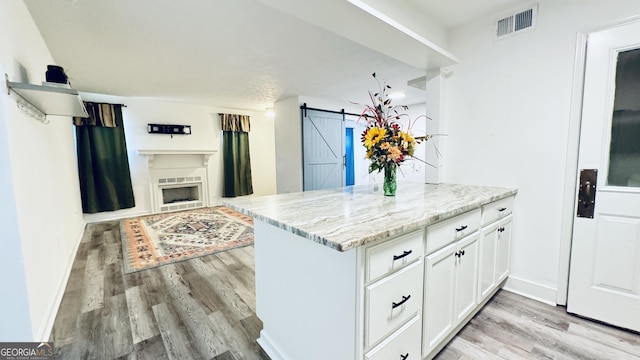 kitchen featuring white cabinets, a barn door, kitchen peninsula, light stone countertops, and light wood-type flooring