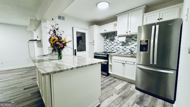 kitchen with stainless steel appliances, light stone countertops, white cabinets, decorative backsplash, and light wood-type flooring