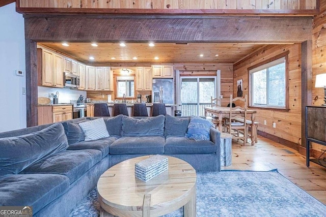 living room featuring wood ceiling, light wood-type flooring, sink, and wooden walls