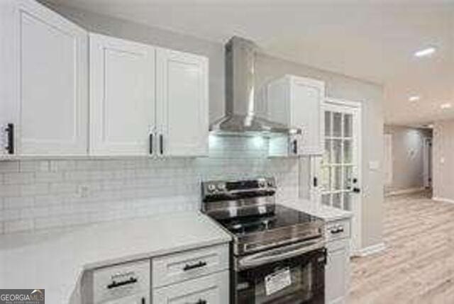 kitchen featuring white cabinets, backsplash, electric range, wall chimney range hood, and light wood-type flooring