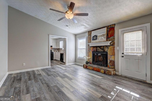 unfurnished living room with a stone fireplace, a textured ceiling, a wealth of natural light, and vaulted ceiling