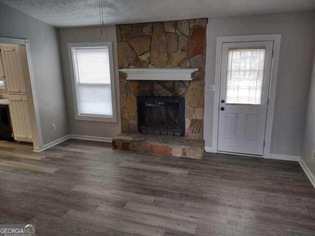 unfurnished living room featuring a textured ceiling, dark hardwood / wood-style floors, and a stone fireplace