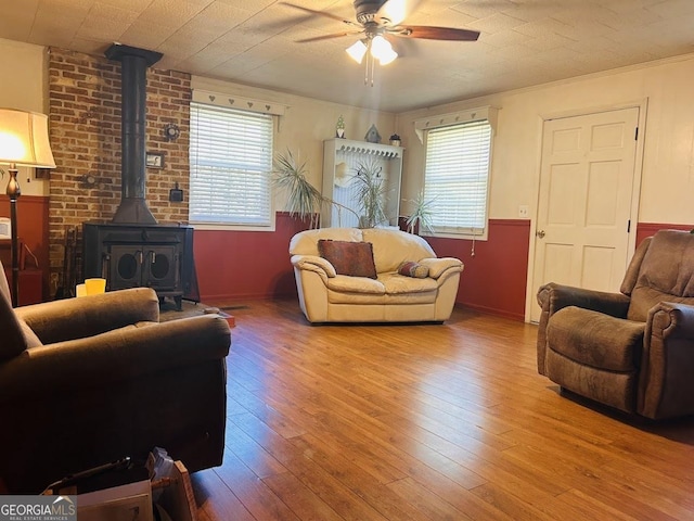 living room featuring a wood stove, ceiling fan, plenty of natural light, and wood-type flooring