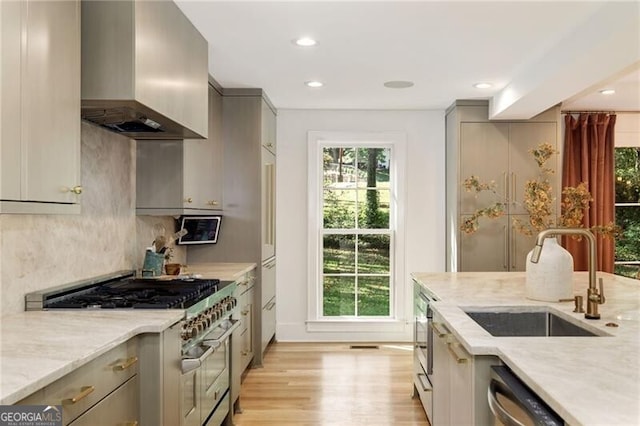 kitchen with light stone counters, gray cabinetry, stainless steel appliances, sink, and wall chimney range hood