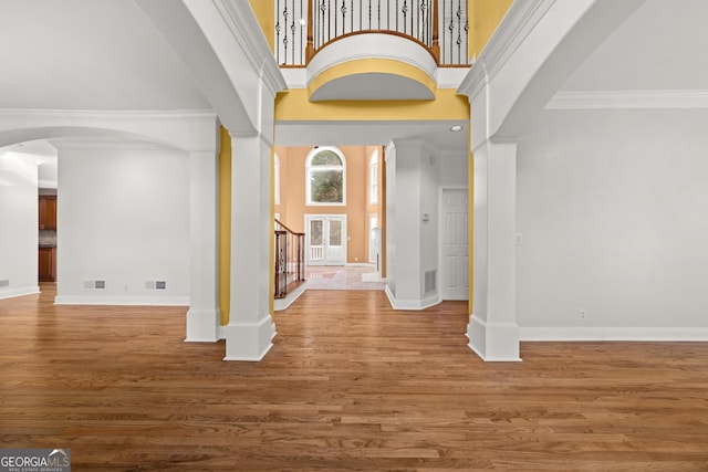 foyer with a high ceiling, decorative columns, ornamental molding, and wood-type flooring