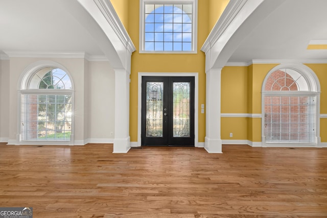 entrance foyer with crown molding, french doors, a towering ceiling, and light hardwood / wood-style floors