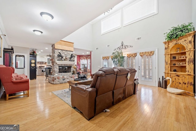 living area featuring light wood-style flooring, crown molding, and a stone fireplace