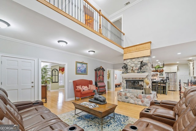 living area featuring a fireplace, visible vents, light wood-style flooring, and ornamental molding