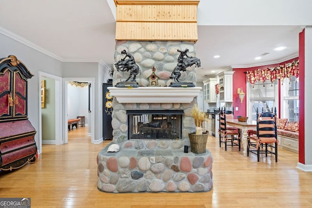 living area featuring a fireplace, baseboards, light wood-style floors, and crown molding