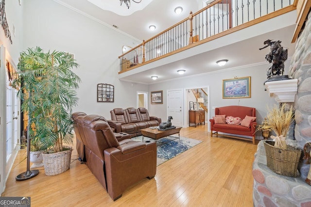 living room featuring a towering ceiling, a fireplace with raised hearth, wood finished floors, ornamental molding, and visible vents