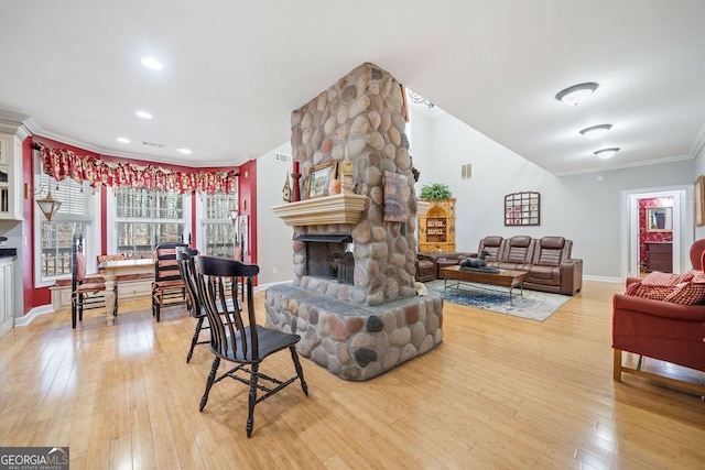 living area with a stone fireplace, baseboards, ornamental molding, visible vents, and light wood finished floors