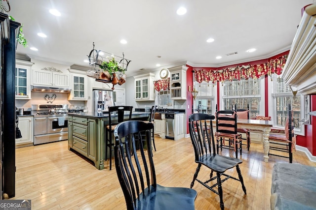 kitchen featuring light wood finished floors, dark countertops, glass insert cabinets, stainless steel appliances, and green cabinetry