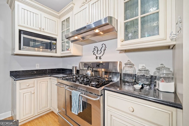 kitchen with glass insert cabinets, stainless steel appliances, extractor fan, and dark stone counters