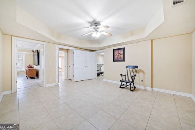 unfurnished room with light tile patterned floors, visible vents, baseboards, a ceiling fan, and a tray ceiling