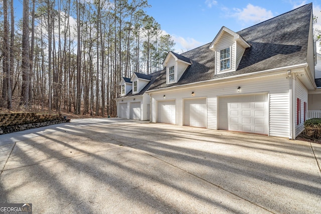 view of side of property featuring driveway, a garage, and roof with shingles