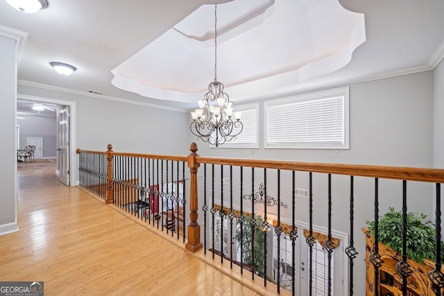 hall with visible vents, a raised ceiling, ornamental molding, light wood-style floors, and a chandelier