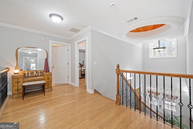 hallway featuring visible vents, ornamental molding, wood finished floors, and an upstairs landing