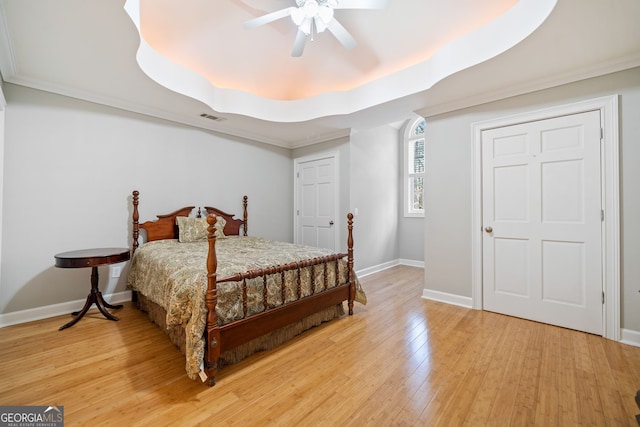 bedroom with baseboards, visible vents, a tray ceiling, and light wood finished floors