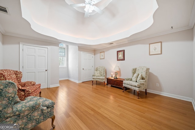 sitting room featuring light wood-style floors, baseboards, visible vents, and a raised ceiling