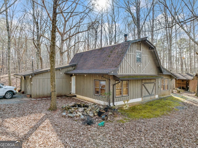 view of side of property featuring driveway, a barn, a gambrel roof, and roof with shingles