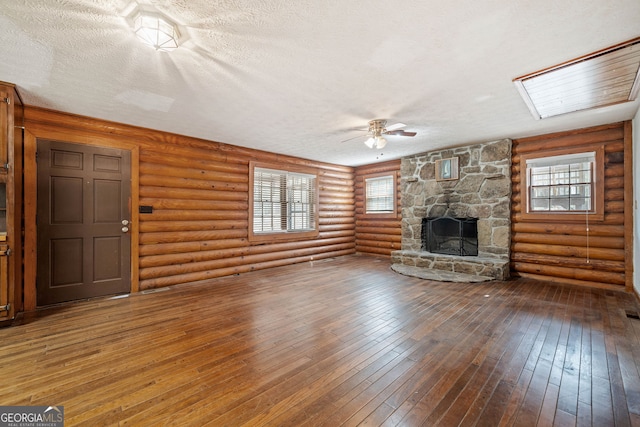 unfurnished living room featuring a ceiling fan, wood finished floors, log walls, a textured ceiling, and a stone fireplace