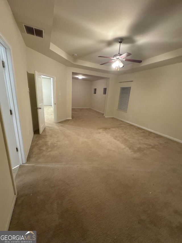 spare room with a tray ceiling, light colored carpet, and ceiling fan