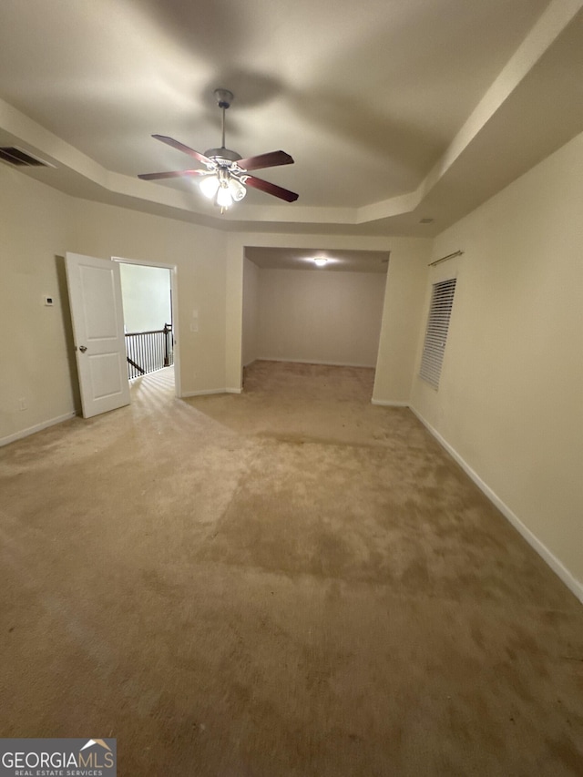 interior space with ceiling fan, a tray ceiling, and carpet flooring